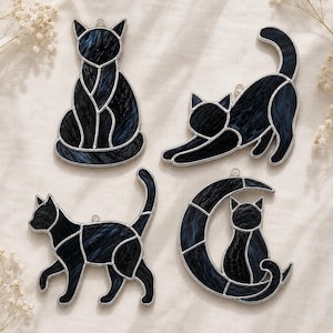 Könnte beinhalten: Vier Buntglas-Katzenanhänger aus dunkelblauem und schwarzem marmoriertem Glas mit silbernen Metalllötlinien. Das Set besteht aus einer sitzenden Katze, einer sich streckenden Katze, einer laufenden Katze und einer Katze in einer Mondsichel.