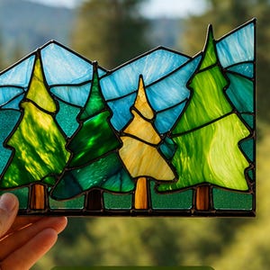 Könnte beinhalten: Glasfenster mit einer Waldszene mit vier Bäumen in Grün- und Gelbtönen, vor blauem Himmel und Bergen. Das Panel wird vor einem verschwommenen grünen Hintergrund gehalten.