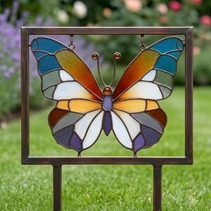 May include: A colorful stained-glass butterfly garden stake. The butterfly features a mosaic design with shades of blue, orange, yellow, white, and purple. The metal frame and stake are a dark bronze color, perfect for outdoor decor.
