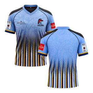 May include: A light blue V-neck sports jersey featuring a gradient pattern with vertical yellow, white, and dark blue stripes at the bottom. The shirt displays the Antigua and Barbuda Falcons logo, text, and various sponsor patches on the sleeves and chest.