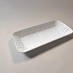 Puede incluir: Una bandeja rectangular blanca con un diseño de tejido de mimbre en los bordes. El centro de la bandeja es liso y plano. La bandeja está hecha de un material brillante y está vacía.