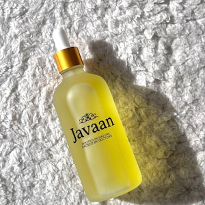 Puede incluir: Una botella de vidrio transparente con un líquido amarillo, un cuentagotas blanco y una tapa dorada. La botella tiene la palabra "Javaan" en negro, con el texto "ROOTED IN NATURE BACKED BY DOCTORS" debajo.