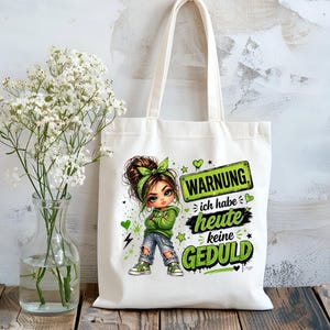 Könnte beinhalten: Weißer Stoffbeutel mit einer Cartoon-Illustration eines Mädchens in einem grünen Kapuzenpullover und Jeans. Der Beutel trägt den Text "WARNUNG ich habe heute keine GEDULD" in Grün und Weiß. Der Beutel hat zwei Griffe.