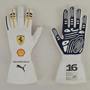 Peut inclure: Paire de gants de course blancs avec le logo Ferrari, le logo Shell et le logo Puma. Les gants ont des accents jaunes et bleu marine, avec le numéro 16 sur le poignet. Conçus pour la course professionnelle.
