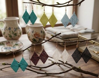May include: Seven pairs of diamond-shaped beaded earrings in teal, lime green, light blue, dark red, white, and black, hanging from branches. A small rectangular plaque at the bottom displays the text: АРТ-БІСЕР: КОЛЕКЦІЯ РОМБІВ.
