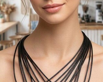 May include: A multi-strand black cord necklace featuring ten heart-shaped pendants in various colors, including red, green, blue, light blue, clear, yellow, purple, pink, and black, each attached with a silver-toned metal bail.