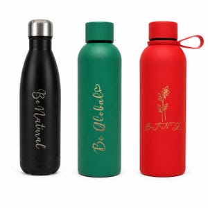 Puede incluir: Tres botellas de agua aisladas en negro, verde y rojo. La botella negra tiene el texto "Be Natural" en letras doradas. La botella verde tiene "Be Global" en letras doradas. La botella roja tiene un diseño floral dorado y el texto "B.T.N.G."