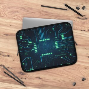 May include: A black laptop sleeve featuring a circuit board design in blue and green. The sleeve has a zip closure and is on a wooden surface with a laptop partially visible.