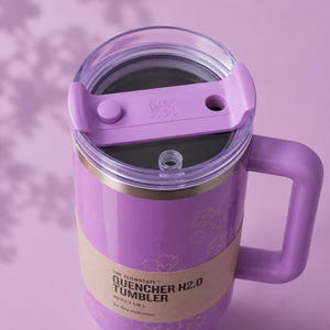 May include: A lilac Stanley Quencher H2.0 tumbler with a handle and clear lid. The tumbler has a capacity of 1.18 L and features a floral design. The text "THE FLOWSTATE QUENCHER H2.0 TUMBLER" is printed on the side.