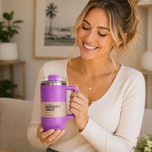 May include: A purple insulated tumbler with a handle and a clear lid. The tumbler has a label that reads "QUENCHER H2.0 TUMBLER". The tumbler is held by a person wearing a white long-sleeved shirt.