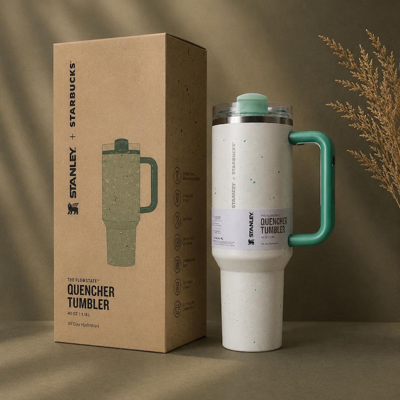 Puede incluir: Un vaso Stanley + Starbucks Quencher salpicado blanco y verde con un asa y tapa verdes. El vaso es de 1,18L y viene con una caja a juego. La caja presenta los logotipos de Stanley y Starbucks y las palabras "The Flowstate Quencher Tumbler".