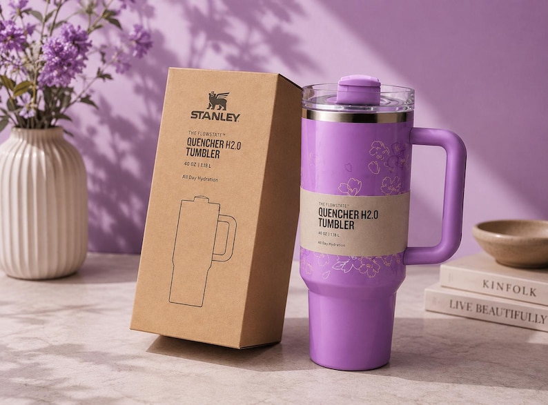 May include: A lilac Stanley Quencher H2.0 tumbler with a handle and a matching box. The tumbler has a floral design and holds 1.18L of liquid. The box features the Stanley logo and product details.