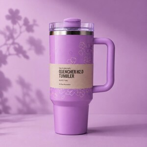 May include: A lilac-coloured tumbler with a handle and a clear lid. The tumbler has a gold rim and a band of text that reads "QUENCHER H2.0 TUMBLER". The tumbler is decorated with a floral design and is designed to hold 1.18 L of liquid.