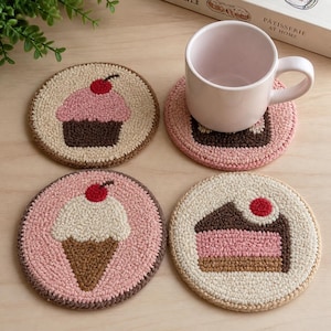 Op de afbeelding: Set van vier ronde, met de hand gestikte onderzetters met dessertontwerpen. Elke onderzetter heeft een ander ontwerp: een cupcake, een stuk cake en een ijsje, allemaal bekroond met een rode kers. De onderzetters zijn in tinten roze, bruin en beige.
