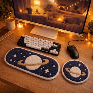 May include: A desk setup featuring a keyboard, mouse, and two navy blue, planet-themed rugs. The rugs have a white planet with a tan ring and white stars. A computer monitor and a mug of coffee are also visible.