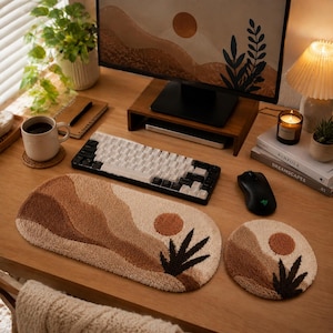 Può includere: Un poggiapolsi per tastiera trapuntato e un tappetino per mouse circolare abbinato, entrambi caratterizzati da un design paesaggistico testurizzato nei toni del crema, beige e marrone scuro, con un sole e sagome di piante su una scrivania.