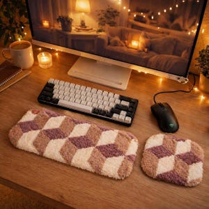 May include: A cozy desk setup featuring a white and black mechanical keyboard, a black mouse, and a matching plush keyboard and mouse pad set with a geometric pattern in shades of cream, mauve, and brown. The desk is made of wood.