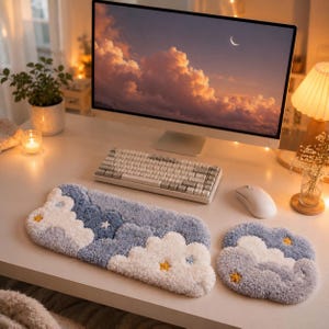 May include: A rectangular keyboard wrist rest and a matching square mouse pad, both featuring a tufted, plush texture with a blue and white cloud pattern and small yellow star accents, positioned on a desk in front of a computer monitor.