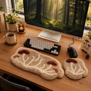 May include: A tufted beige keyboard wrist rest and a matching mouse pad, both featuring a raised, textured design of brown mushrooms with cream-colored stems. The items are placed on a wooden desk in front of a computer monitor and keyboard.