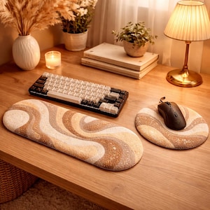 May include: A wooden desk setup featuring a beige and brown patterned keyboard wrist rest and mouse pad. A black and white mechanical keyboard and a black mouse are also on the desk. The desk is lit by a warm-toned lamp.
