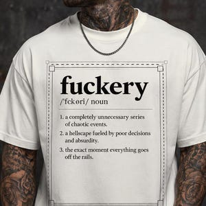May include: An off-white short-sleeve t-shirt featuring a black graphic print of a dictionary-style definition for the word "fuckery." The text includes phonetic pronunciation and three numbered definitions describing chaotic events and poor decisions.