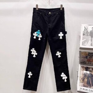May include: Black corduroy pants with white cross appliques. One cross is light blue. The pants have a classic five-pocket design and a button and zipper closure. The pants are hanging on a hanger.