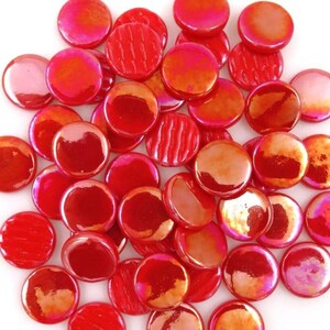 May include: A collection of circular glass cabochons in various shades of red, featuring a glossy, iridescent finish. Some pieces display a smooth, reflective surface, while others show subtle vertical line textures across their rounded tops.