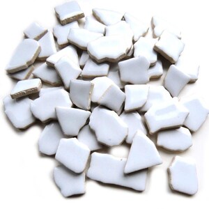 May include: A collection of irregularly shaped, white ceramic tile pieces with light brown edges. The pieces vary in size and shape, creating a mosaic effect. The tiles are scattered, suggesting a craft or DIY project.