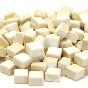 May include: A pile of small, off-white, square-shaped objects. The objects have a slightly textured surface and appear to be stacked randomly. The lighting is bright, and the background is plain white.