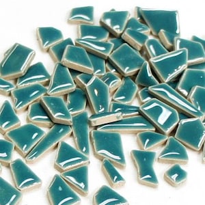 May include: A collection of teal-colored mosaic tiles in various shapes and sizes. The tiles have a glossy finish and are scattered across a white surface. Ideal for craft projects, these tiles offer a vibrant color and unique texture.