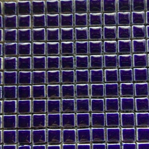 May include: Close-up of a grid of small, square tiles. Each tile is a deep, glossy blue with a white border. The tiles are evenly spaced, creating a repeating pattern. The overall effect is a textured, mosaic-like surface.