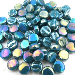 May include: A collection of small, round, flat glass cabochons featuring a glossy, iridescent teal finish. Each piece displays a smooth, domed surface with reflective highlights in shades of blue, green, and gold, creating a shimmering effect.