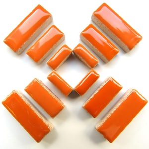 May include: Orange rectangular ceramic tiles with a glossy finish and a beige base are arranged on a white surface. The tiles are in various orientations, showcasing their shape and color. These tiles are suitable for mosaic projects.