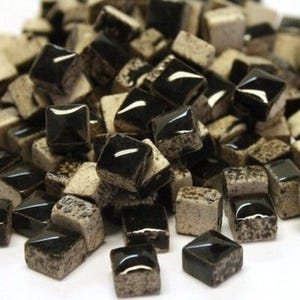 May include: A pile of small, square mosaic tiles. The tiles are a mix of glossy black and speckled beige. The black tiles have a shiny, reflective surface, while the beige tiles have a textured, matte appearance. These tiles are suitable for various craft projects.