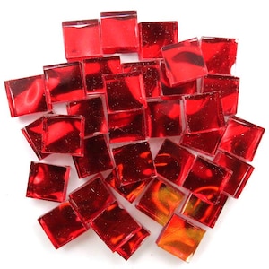 May include: A collection of small, square, red glass tiles. The tiles are arranged in a loose pile, with varying shades of red and a glossy finish. The tiles are likely for mosaic art or craft projects.