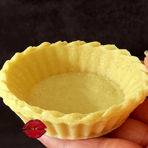 May include: A pale yellow, round pastry tart shell with a fluted, crimped edge. The dough has a smooth, matte texture and a consistent thickness throughout the base and sides. A small red logo with the text Lilliz Classic is visible.