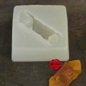 May include: A white silicone mold with a rectangular base and a diagonal, hollowed-out cavity shaped like a pastry. Beside the mold sits a golden-brown, fried pastry shell. A small red logo with the text Lillie Classic is visible.