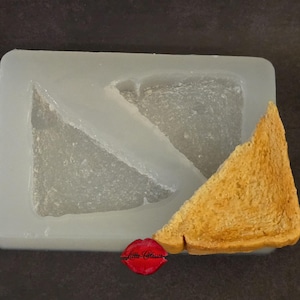 May include: A rectangular, translucent silicone mold featuring two triangular cavities designed for crafting. Beside the mold sits a single, realistic, golden-brown triangular piece of toasted bread with a textured, porous surface.