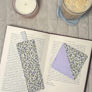 May include: A rectangular fabric bookmark with a white lace tab and a triangular corner bookmark, both featuring a floral pattern of small purple flowers and green leaves on a white background. The corner bookmark has a solid light purple fabric interior.