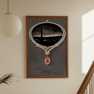 Op de afbeelding: Een ingelijste print met een kettingontwerp met een silhouet van een stadsgezicht. De ketting is versierd met diamanten en een grote rode edelsteen. De print staat tegen een grijze achtergrond, met tekst onderaan. De lijst is bruin.