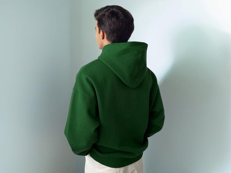 Puede incluir: Una sudadera con capucha de color verde bosque s&oacute;lido con mangas largas, capucha sin cordones y dobladillo acanalado. La prenda se muestra desde la parte posterior, exhibiendo un dise&ntilde;o liso sin patrones con un ajuste relajado y textura mate.