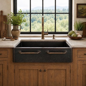 May include: A dark, hammered copper farmhouse sink featuring two horizontal metal handles on the front apron. The sink is set into a light-colored countertop above wooden cabinets, with a tall, brass-toned faucet centered behind the basin.