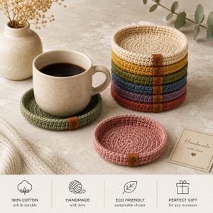 May include: A set of round, crocheted cotton coasters in various colors including beige, yellow, green, blue, purple, red, and pink. Each coaster features a small brown leather tag with a leaf icon. One green coaster holds a ceramic mug.