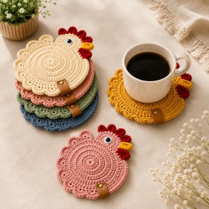 May include: A set of round, crocheted chicken-shaped coasters in cream, pink, green, blue, and yellow. Each coaster features a scalloped edge, a red and yellow comb, a single eye, and a small brown leather tab with a metal rivet at the base.