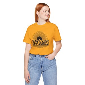 May include: Mustard yellow t-shirt with a black graphic of a sun rising over geometric mountain shapes. The shirt is short-sleeved and worn with blue denim jeans. The design is a nature-inspired graphic tee.