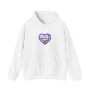 Op de afbeelding: Witte hoodie met een voorzak en een capuchon met trekkoord. De hoodie heeft een hartvormige afbeelding met de woorden "Certified Hater" in een retro lettertype, omlijnd in roze en blauw.