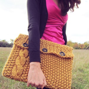 May include: A mustard yellow knitted clutch bag with a flap closure and three brown buttons. The bag is made with a cable knit pattern.