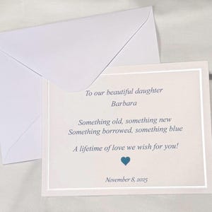 Op de afbeelding: Een witte rechthoekige kaart met een zilveren rand en een bijpassende witte envelop. De kaart bevat blauwe tekst met de tekst: To our beautiful daughter Barbara, Something old, something new, Something borrowed, something blue, A lifetime of love we wish for you!, een blauw hartsymbool en de datum 8 november 2025.