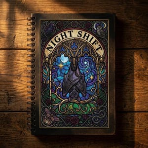 Könnte beinhalten: Ein spiralgebundenes Notizbuch mit dunkelbraunem Einband. Das Cover zeigt ein Buntglasdesign mit einer Fledermaus, einem Mond, Sternen und dem Schriftzug "NIGHT SHIFT". Der Hintergrund ist eine Mischung aus Blau- und Lilatönen.