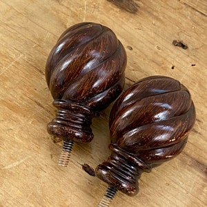 May include: Two dark brown wooden finials with a twisted design. The finials have a threaded metal screw on the bottom.